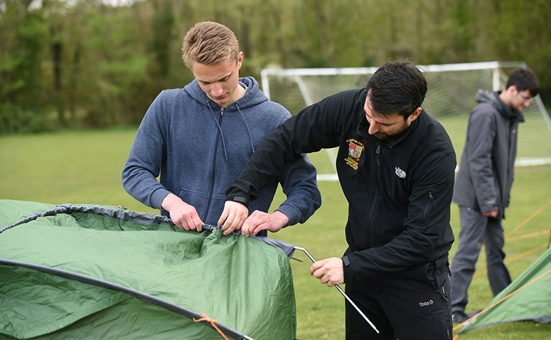 Students setting up a tent, feeding the tent pole through the canvas