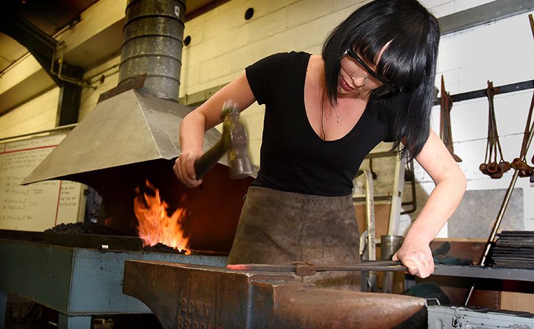 Student working a hot piece of metal with a hammer over an anvil